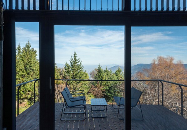 A deck with two chairs and a table, overlooking a forest and mountains.