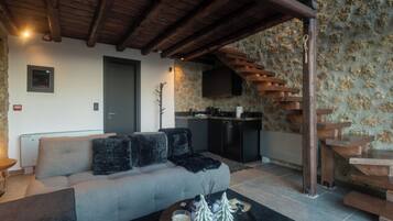 Un salon avec un canapé, une table basse ornée de bougies et un petit sapin de Noël, un coin cuisine avec une cuisinière, et un escalier en bois.