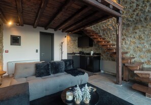 A living room with a sofa, a coffee table with candles and a small Christmas tree, a kitchen area with a stove, and a wooden staircase.