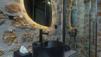 Une salle de bain avec un lavabo rond noir, un miroir et une douche en verre.