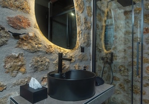A bathroom with a round black sink, a mirror, and a glass shower enclosure.