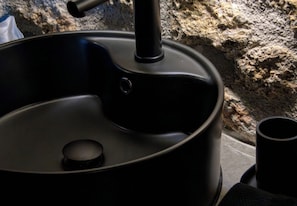 A black outdoor cooking pot with a lid and a handle, placed on a stone surface.