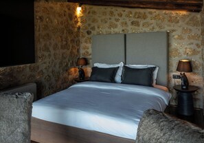 A bedroom with a bed, two bedside tables, a wall-mounted TV, and a stone-patterned wall.