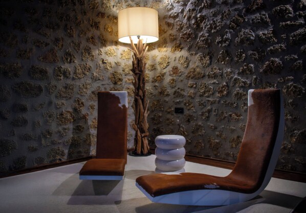 A room with a stone wall, a wooden floor lamp, and two brown cushioned chairs.