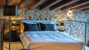 Une chambre avec un mur en pierre, un lit avec une literie blanche et deux lampes de chevet.