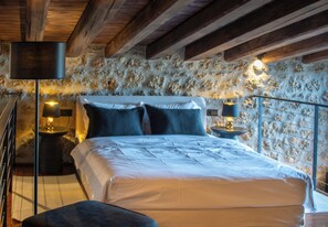 A bedroom with a stone wall, a bed with white bedding, and two bedside lamps.