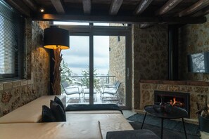 A cozy room with a sofa, a table with a fire, and a balcony with chairs.