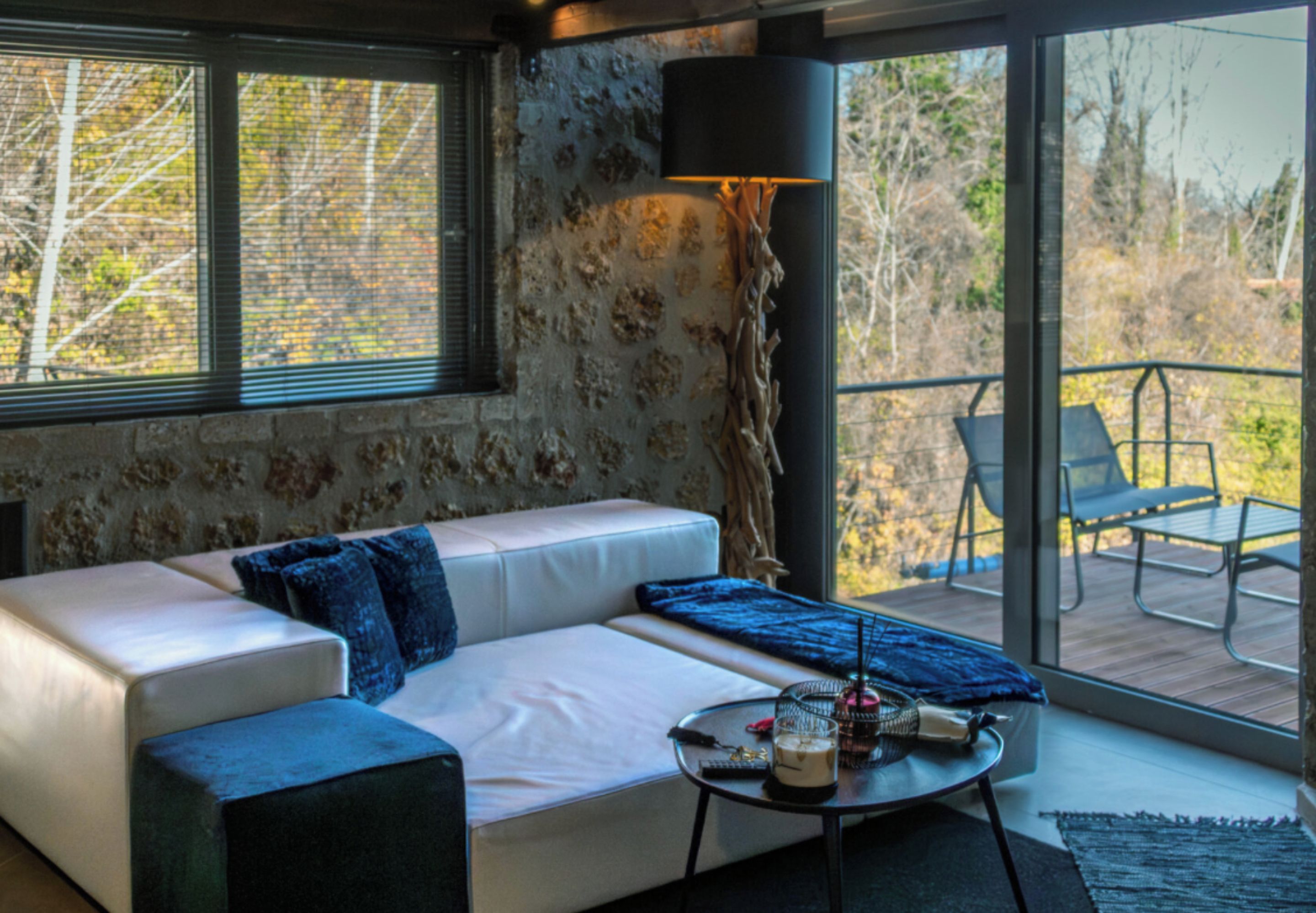 A modern living room with a white sofa, a coffee table, and a view of the outdoors through large windows.