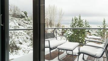 Un balcon avec des chaises en métal et une table recouverte de neige, d’où l’on peut admirer un paysage enneigé et des arbres.