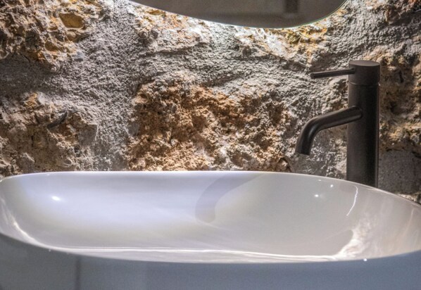 A bathroom with a white sink, a black faucet, and a stone wall.