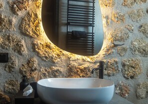 A bathroom with a stone wall, a round sink, and a mirror with a towel rack.