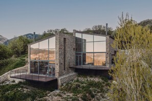Ein modernes Haus mit großen Glasfenstern, einer Steinaußenwand und einer Holzterrasse.