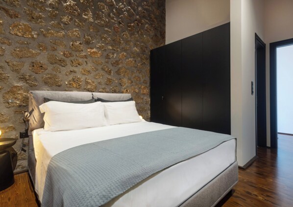 Ein Schlafzimmer mit einem Bett, einer Steinwand, einem dunklen Kleiderschrank und einem Holzboden.