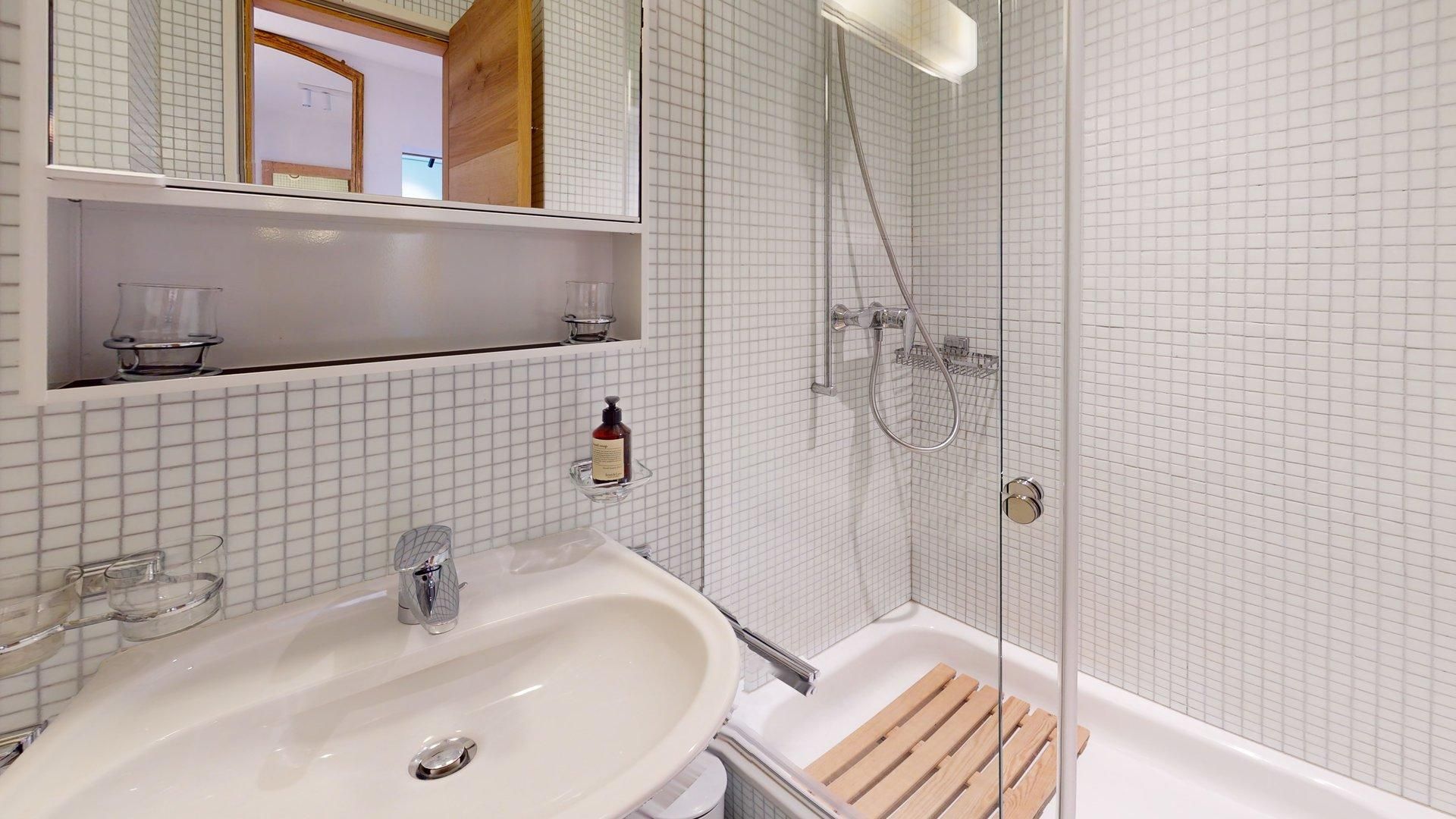 A bathroom with a white sink, a glass shower enclosure, and a wooden bath mat.