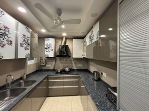 A modern kitchen with a central island, stainless steel appliances, and decorative wall tiles. - Fortune Home Service Apartment 3BHK M112 (New Delhi)
