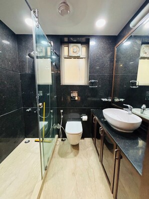 Uma casa de banho moderna com cabine de duche em vidro, sanita branca e uma grande pia.