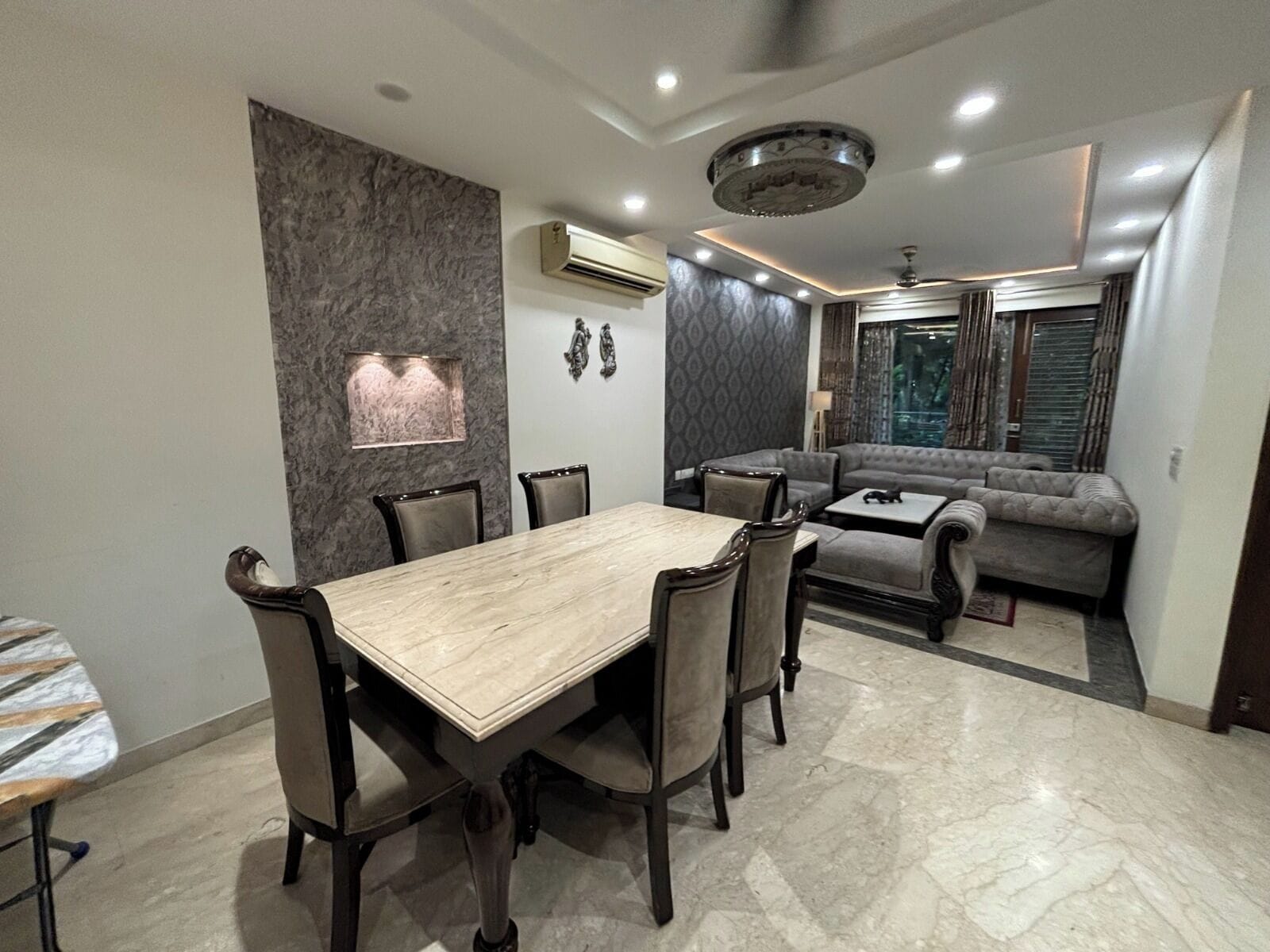 A modern dining area with a marble table and chairs, a sofa, and a decorative wall.