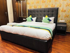 A hotel room with a large bed, a dark headboard, and a floral wallpaper pattern. - Fortune Home Service Apartment 3BHK M112 (New Delhi)