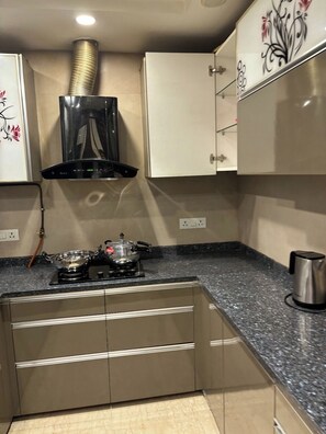 A kitchen with a gas stove, a coffee maker, and a stainless steel kettle on the counter. - Fortune Home Service Apartment 3BHK M112 (New Delhi)