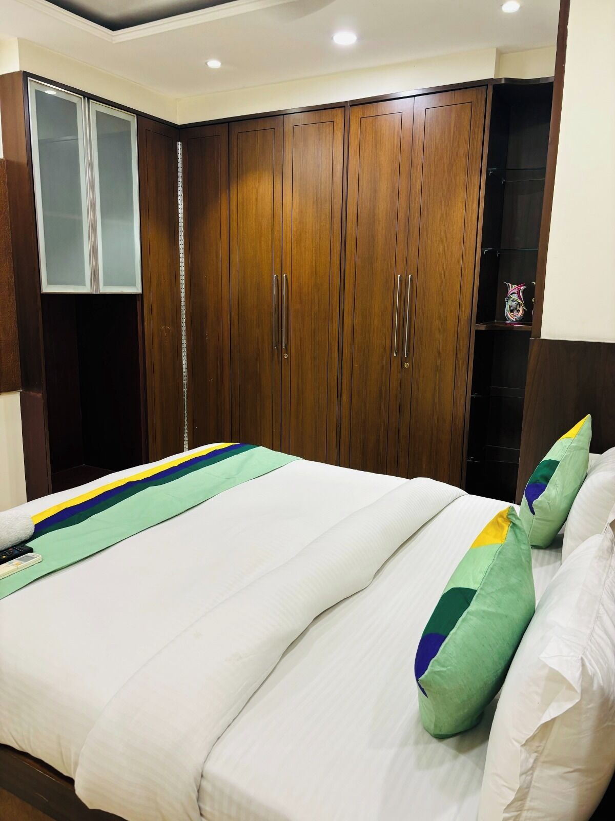 Una habitación de hotel con una cama grande, un armario de madera y un pequeño estante.