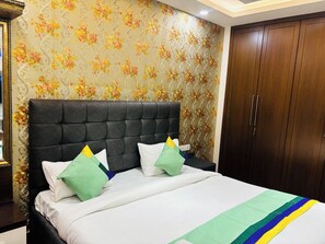 A bedroom with a tufted headboard, a bed with white bedding and green pillows, and a wooden wardrobe. - Fortune Home Service Apartment 3BHK M112 (New Delhi)