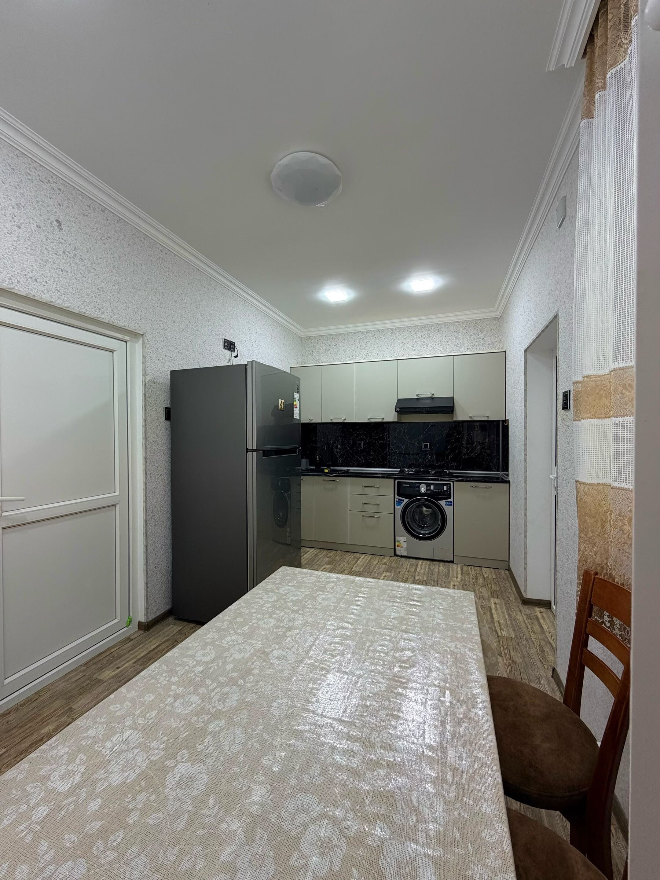 A compact kitchen with a refrigerator, washing machine, and a dining table with chairs.