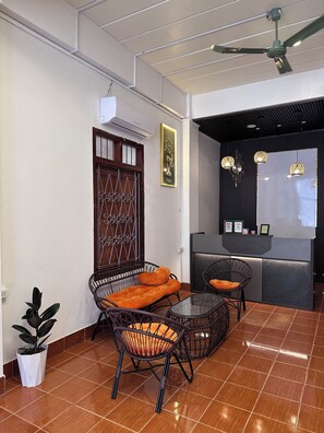 A room with a reception desk, wicker furniture, a ceiling fan, and a potted plant. - Green Hill Hostel (Vientiane)