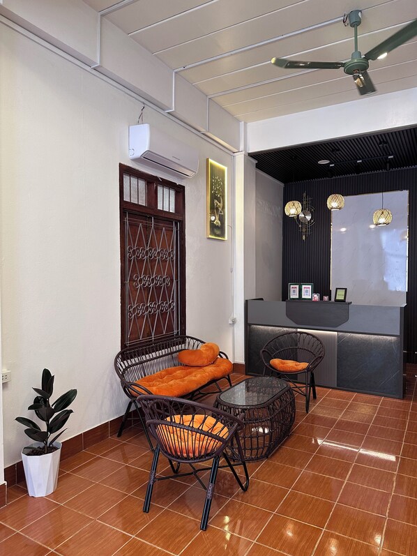 Una habitación con una mesa de recepción, muebles de mimbre, un ventilador de techo y una planta en maceta.