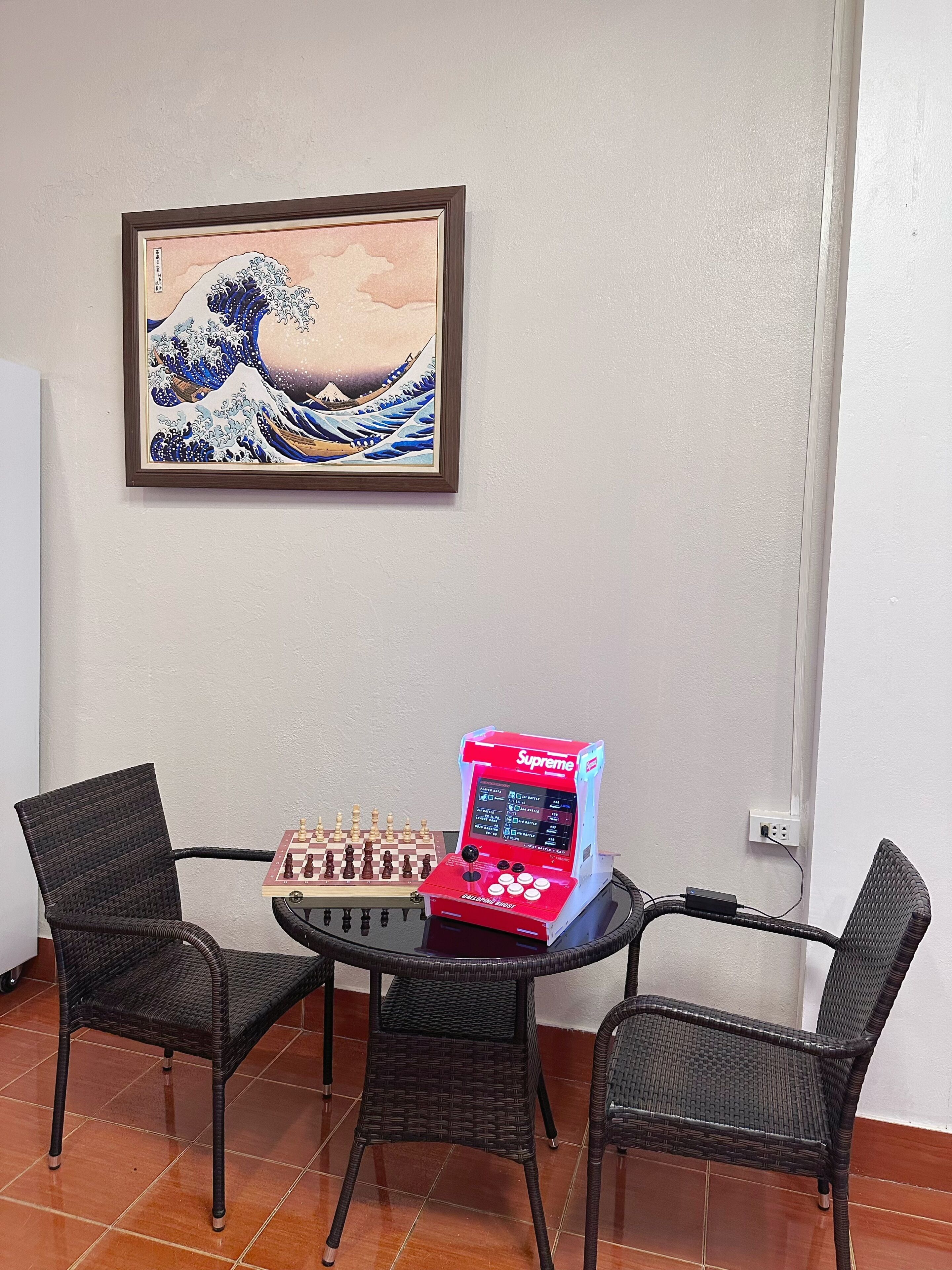 Een kamer met een traditioneel Japans golfschilderij, een schaakbord en een rode elektronische spelconsole.