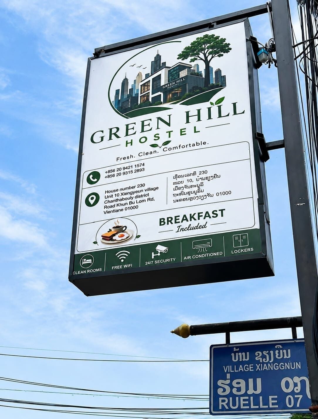A sign for Green Hill Hostel advertising amenities like clean rooms, free WiFi, 24/7 security, air conditioning, and included breakfast.