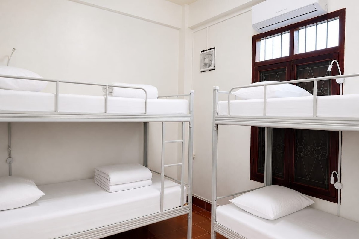 Una habitació de dormitori amb lliteres, una finestra amb marc de fusta i un aparell d'aire condicionat.