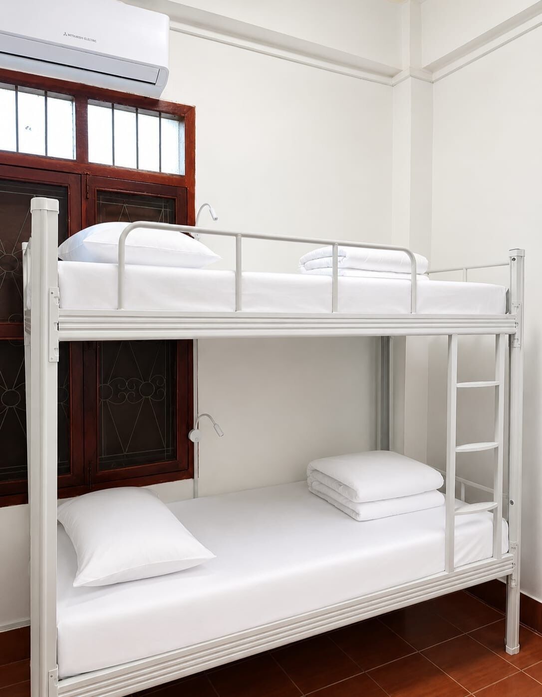 A bunk bed with white bedding, a window with a wooden frame, and an air conditioning unit above.