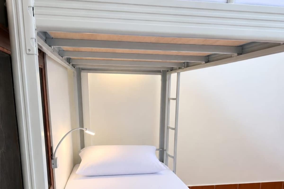 Una cama litera con un colchón individual, una almohada, una lámpara de noche y un suelo de madera.