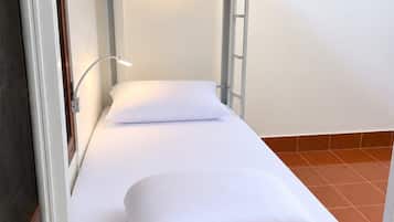 A bunk bed with a single mattress and a pillow, a bedside lamp, and a wooden floor.