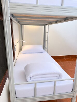 A bunk bed with a single mattress and a pillow, a bedside lamp, and a wooden floor.