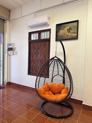 A room with a hanging chair, a door with a decorative glass panel, and an air conditioning unit on the wall.