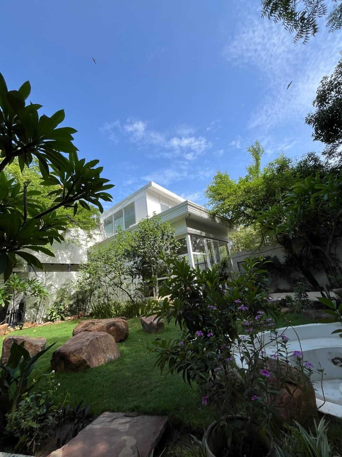 A modern building with a glass facade, surrounded by lush greenery and large rocks.