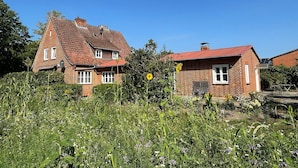 A two-story brick house with a red-tiled roof, surrounded by a garden with various plants and flowers. - Vrbo Property (Bohlsen)