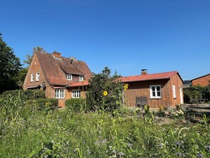 A two-story brick house with a red-tiled roof, surrounded by a garden with various plants and flowers. - Vrbo Property (Bohlsen)