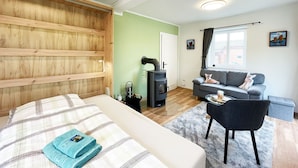 A bedroom with a bed, a wooden headboard, a grey sofa, a black chair, and a window with curtains. - Vrbo Property (Bohlsen)