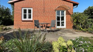 A brick building with a red roof, a window, a door, and a patio with two chairs and a table. - Vrbo Property (Bohlsen)
