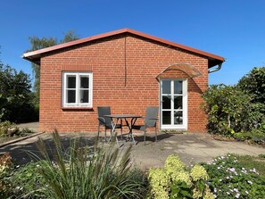 A brick building with a red roof, a window, a door, and a patio with two chairs and a table. - Vrbo Property (Bohlsen)