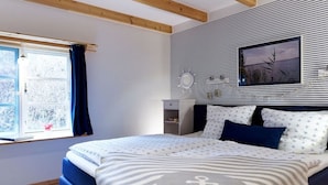 Een slaapkamer met een bed, een raam met gordijnen, een aan de muur hangend schilderij en een houten balk.