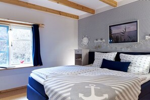 A bedroom with a bed, a window with curtains, a wall-mounted picture, and a wooden ceiling beam. - Holiday home with 1 bedroom (Groß Zecher)