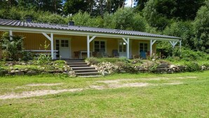 Een gelijkvloers gebouw met een veranda, een trap naar de ingang en een tuin met een stenen muur en treden.