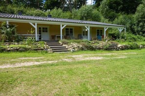 A single-story building with a porch, a set of stairs leading to the entrance, and a garden area with a stone wall and steps. - Holiday home with 1 bedroom (Groß Zecher)
