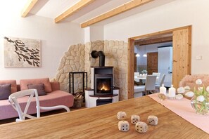 A cozy living room with a stone wall, a fireplace, a dining table with dice, and a sofa. - Holiday home with 1 bedroom (Groß Zecher)