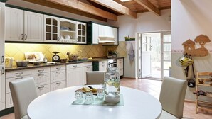 Een keuken met witte kastjes, een ronde eettafel en een hangplant.