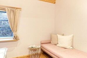A room with a pink sofa, a small side table with a magazine, a window with curtains, and a white chair. - Holiday home with 1 bedroom (Groß Zecher)