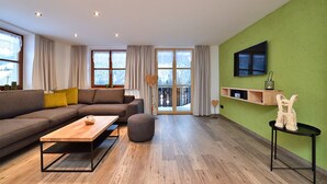 En moderne stue med sofa, sofabord og et fjernsyn ophængt på en grøn væg.